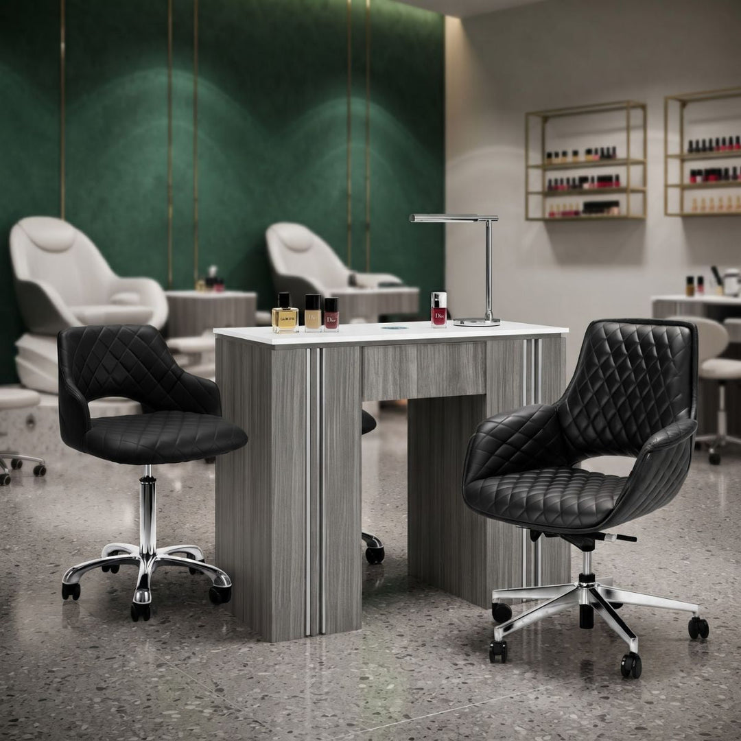 Modern grey wood manicure table with white top and black quilted diamond-stitched technician chairs in a luxury nail salon.