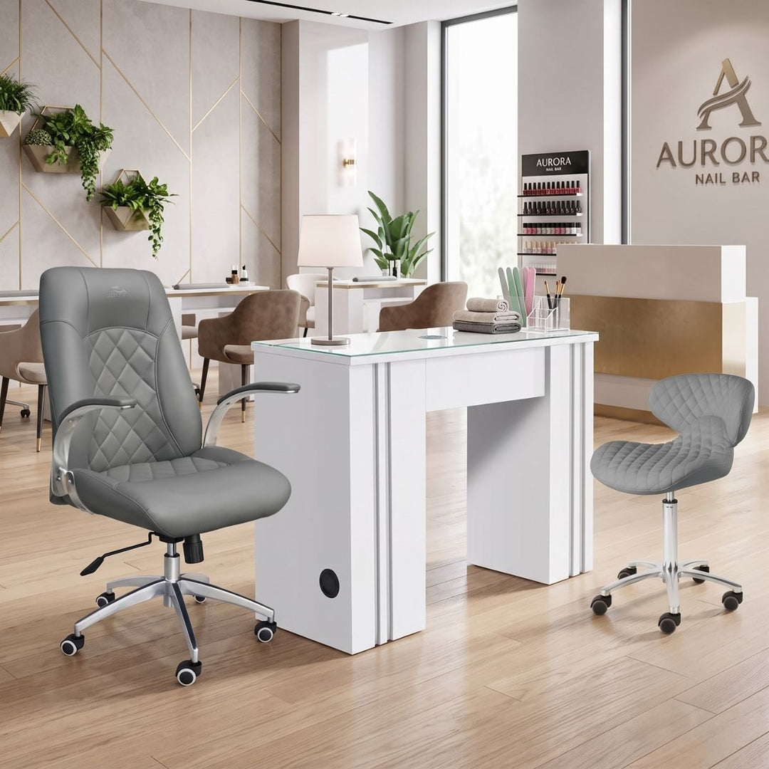 Modern white manicure table station with grey leather client chair and technician stool in a nail salon.