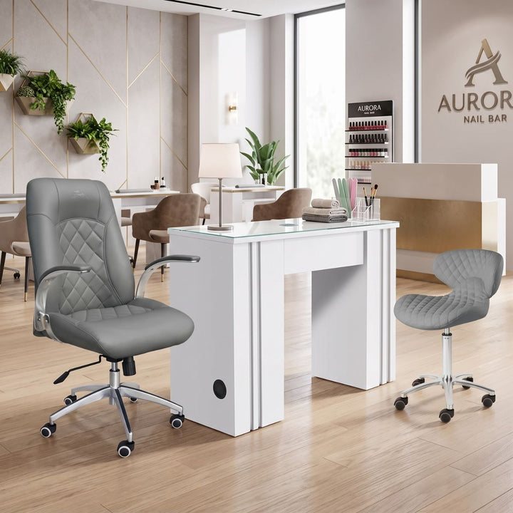 Modern white manicure table station with grey leather client chair and technician stool in a nail salon.